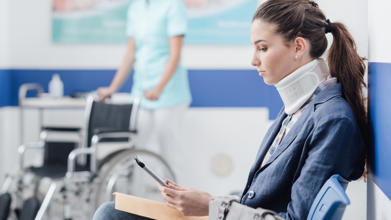 vrouw zit in ziekenhuis te wachten met nekbrace